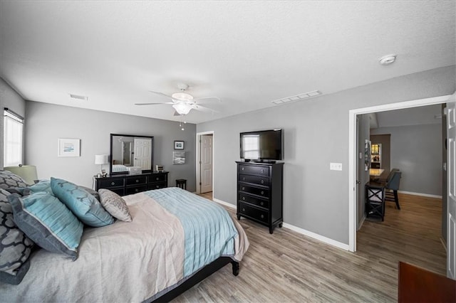 bedroom featuring ceiling fan, light wood-type flooring, visible vents, and baseboards