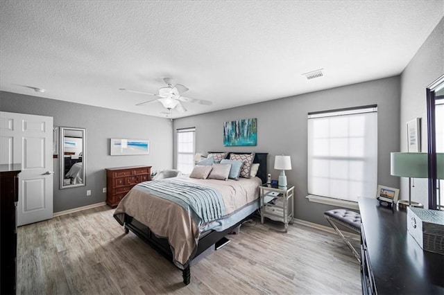 bedroom featuring a textured ceiling, visible vents, baseboards, a ceiling fan, and light wood finished floors