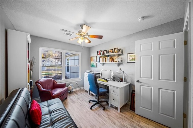 office space with a textured ceiling, light wood-style flooring, visible vents, baseboards, and a ceiling fan