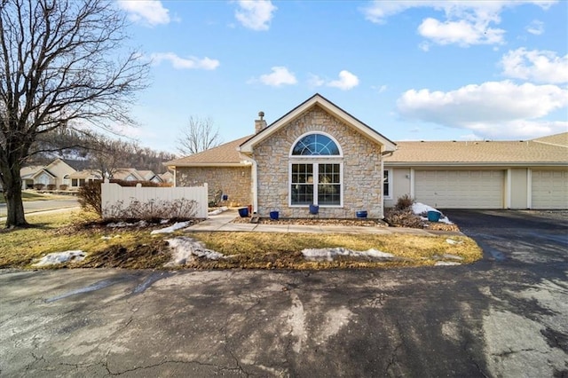 ranch-style house featuring a chimney, an attached garage, fence, stone siding, and driveway