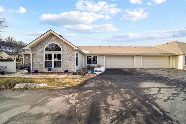 ranch-style house with a garage, fence, driveway, stone siding, and stucco siding