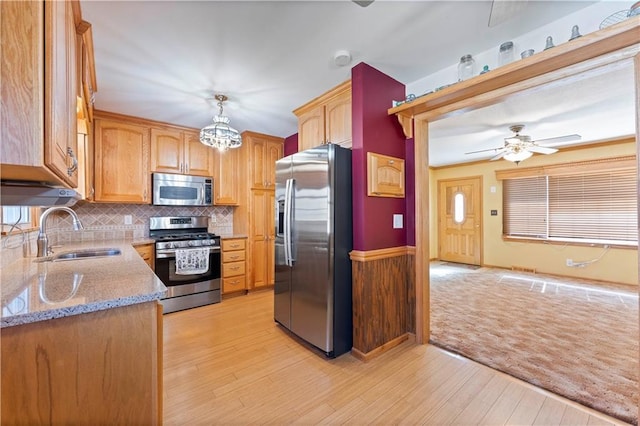 kitchen featuring light wood finished floors, tasteful backsplash, light stone counters, stainless steel appliances, and a sink