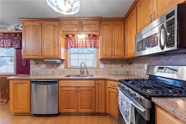 kitchen with light stone countertops, stainless steel appliances, a sink, light wood-type flooring, and decorative backsplash