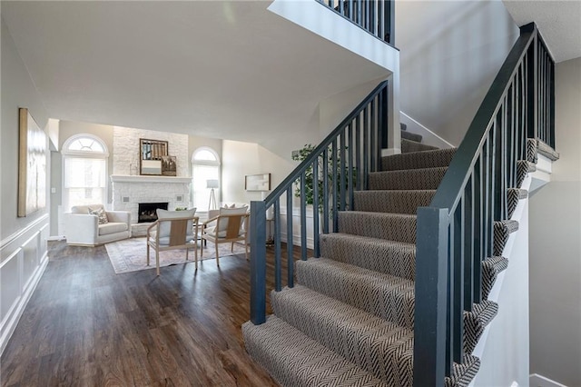 stairs with baseboards, a fireplace, a high ceiling, and wood finished floors