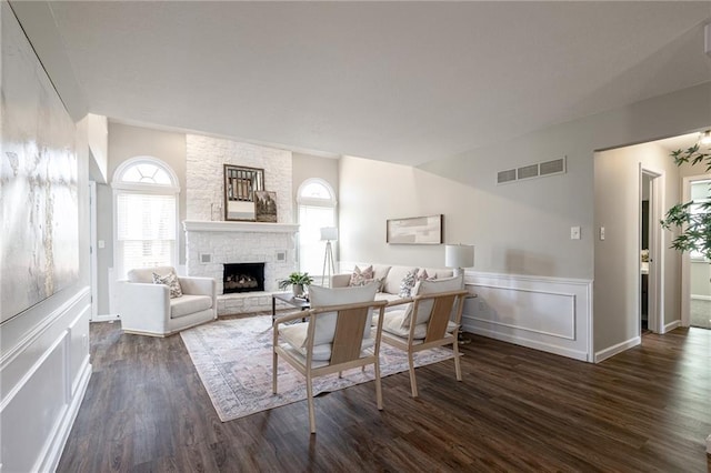 living room with wainscoting, visible vents, dark wood-type flooring, and a stone fireplace