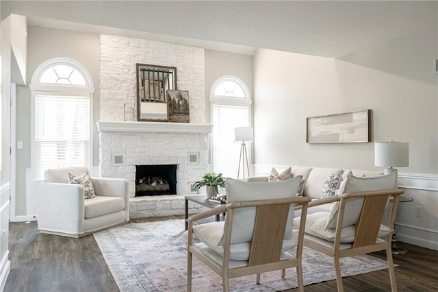 living room featuring a wainscoted wall, wood finished floors, and a stone fireplace