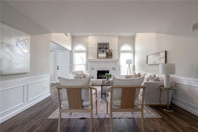 living room with dark wood-style floors, a wealth of natural light, wainscoting, and a stone fireplace