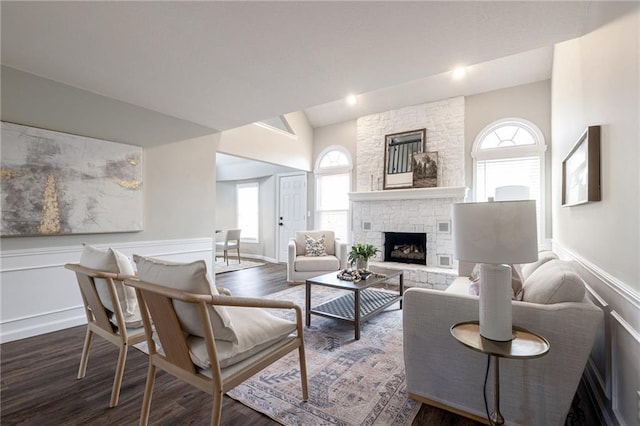 living area with vaulted ceiling, a stone fireplace, wainscoting, and dark wood finished floors