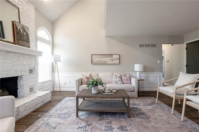 living area featuring a stone fireplace, wainscoting, wood finished floors, and visible vents