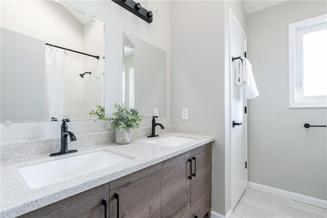 bathroom with double vanity, curtained shower, baseboards, and a sink