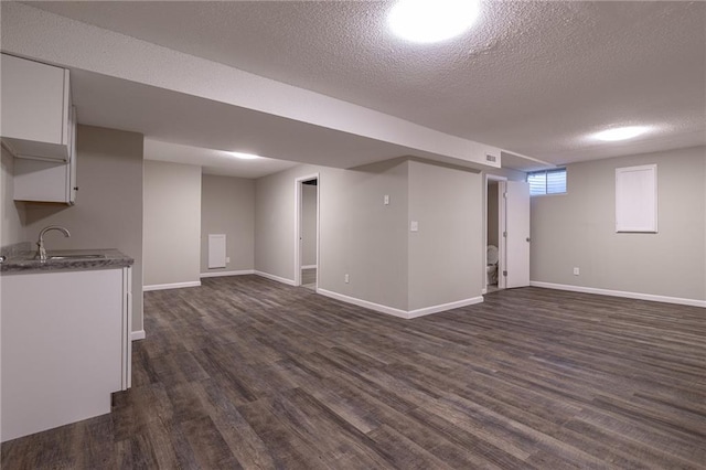 basement featuring dark wood-style floors, a sink, a textured ceiling, and baseboards