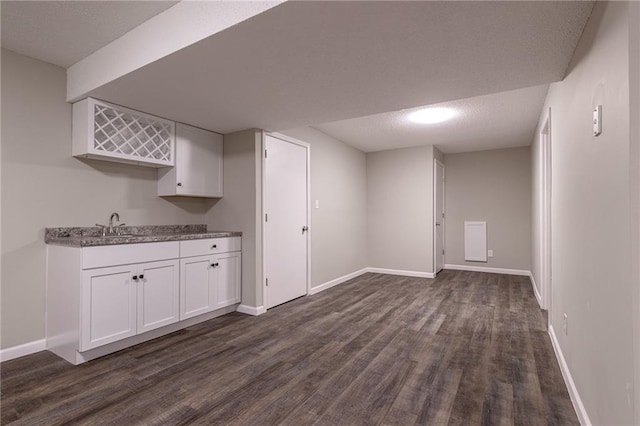 bar featuring a textured ceiling, dark wood-style flooring, a sink, and baseboards