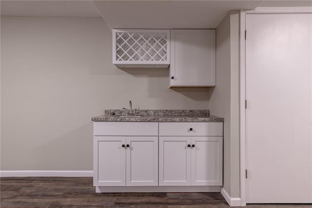 kitchen featuring white cabinets, a sink, baseboards, and light stone countertops