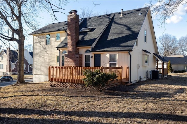 rear view of house with central AC, a chimney, a wooden deck, and roof with shingles