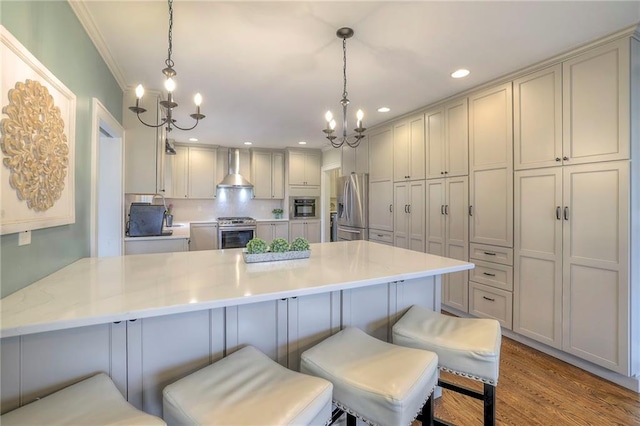 kitchen featuring a notable chandelier, a peninsula, stainless steel appliances, and wall chimney range hood