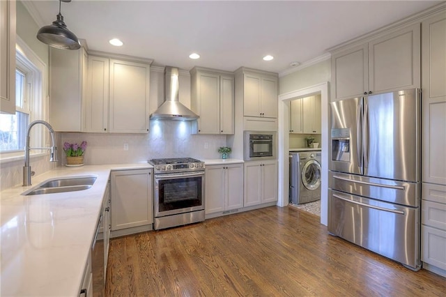 kitchen with wall chimney range hood, dark wood finished floors, stainless steel appliances, washer / clothes dryer, and a sink