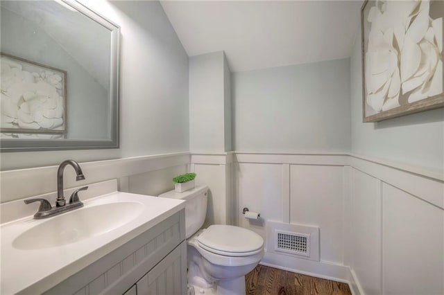 bathroom featuring visible vents, a wainscoted wall, toilet, wood finished floors, and vanity