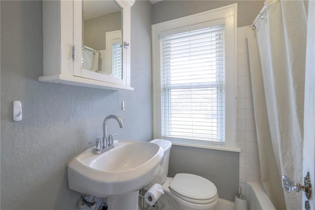 full bathroom with a sink, toilet, shower / tub combo with curtain, and a textured wall