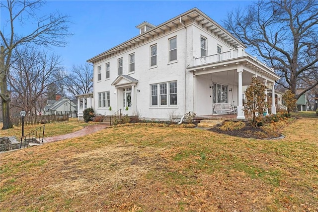 italianate-style house featuring covered porch, a balcony, and a front lawn