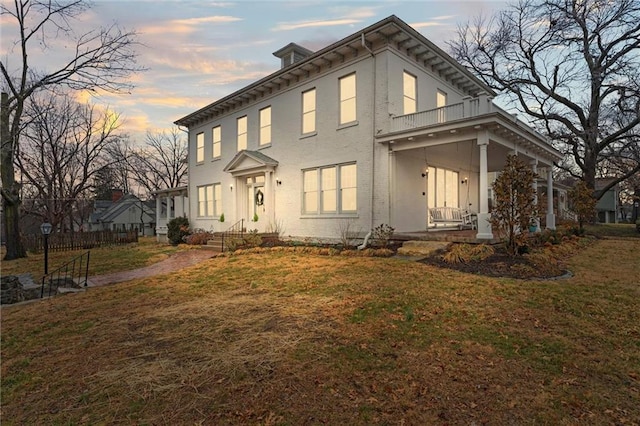 view of front facade featuring covered porch, a balcony, and a front lawn