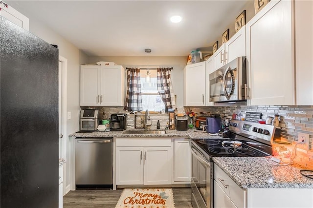 kitchen featuring decorative backsplash, appliances with stainless steel finishes, wood finished floors, white cabinetry, and a sink