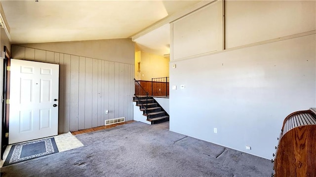 entrance foyer featuring visible vents, stairway, carpet, wood walls, and lofted ceiling