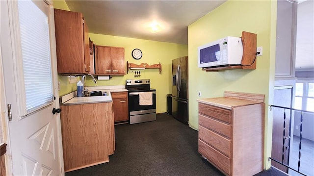 kitchen with a sink, stainless steel appliances, light countertops, brown cabinets, and dark carpet