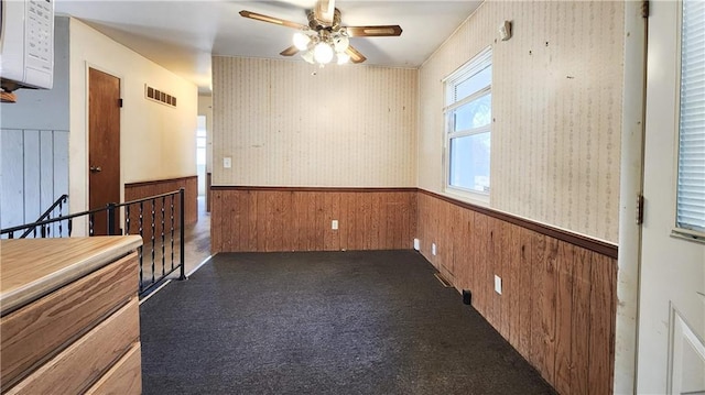 empty room with a wainscoted wall, ceiling fan, wallpapered walls, and visible vents