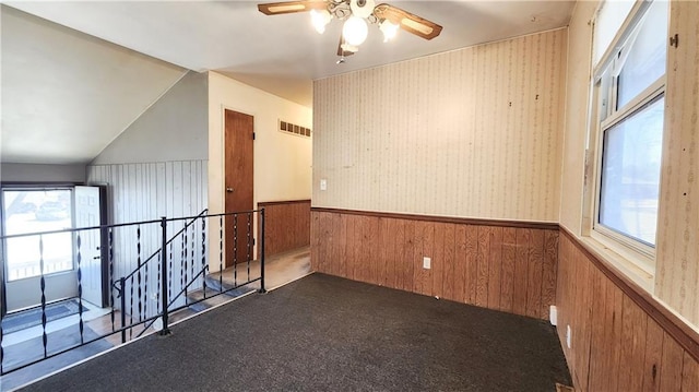 carpeted empty room featuring plenty of natural light, a ceiling fan, visible vents, and wainscoting