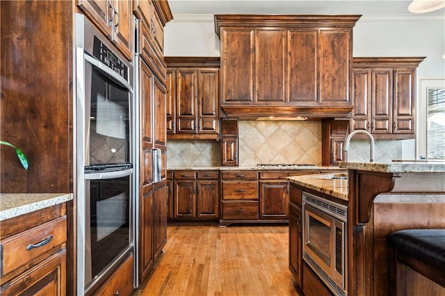 15300 Mastin St, Overland Park, KS 66221 - kitchen featuring crown molding, appliances with stainless steel finishes, light wood finished floors, and ventilation hood