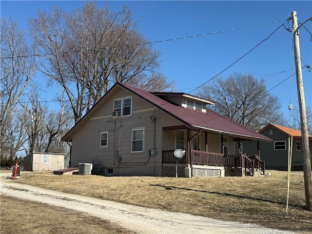 view of property exterior featuring cooling unit, covered porch, metal roof, and an outdoor structure