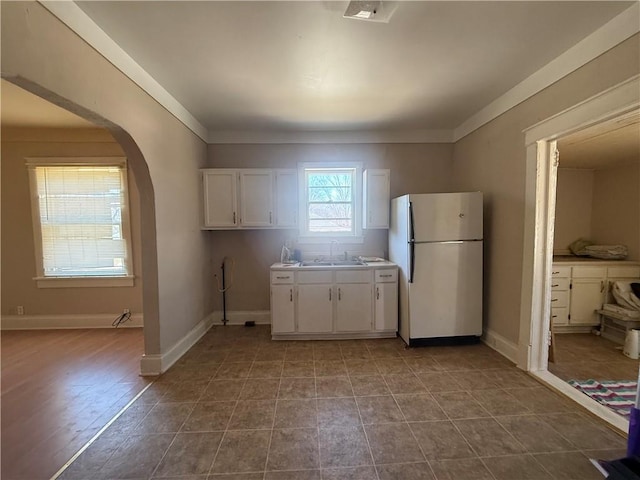 kitchen with arched walkways, baseboards, freestanding refrigerator, and white cabinets