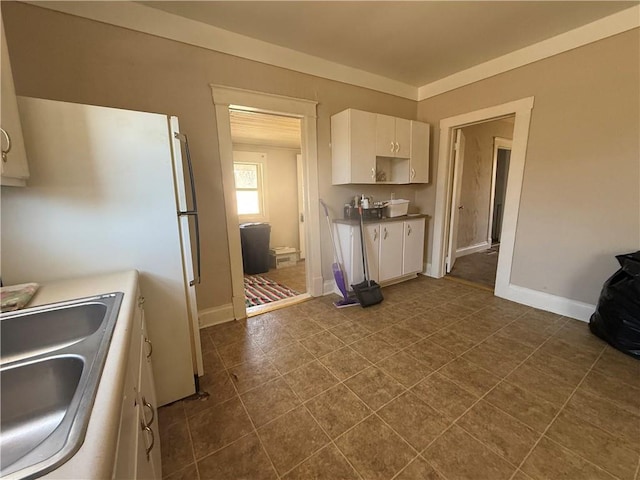 kitchen with dark tile patterned floors, baseboards, white cabinets, and a sink