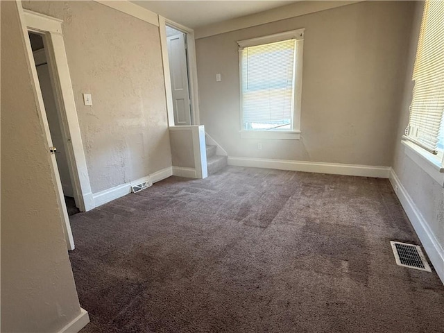 carpeted empty room featuring visible vents, a textured wall, baseboards, and stairs