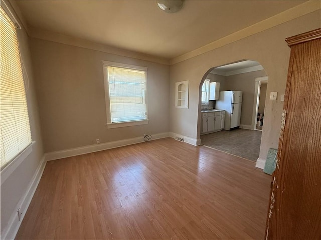 spare room with baseboards, arched walkways, wood finished floors, and ornamental molding