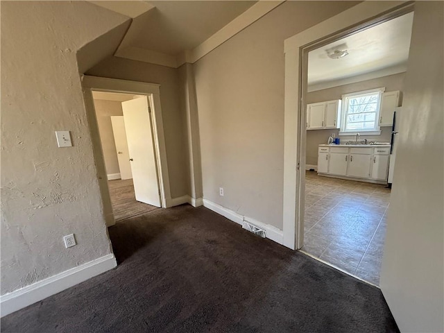 interior space featuring carpet, baseboards, a sink, and a textured wall