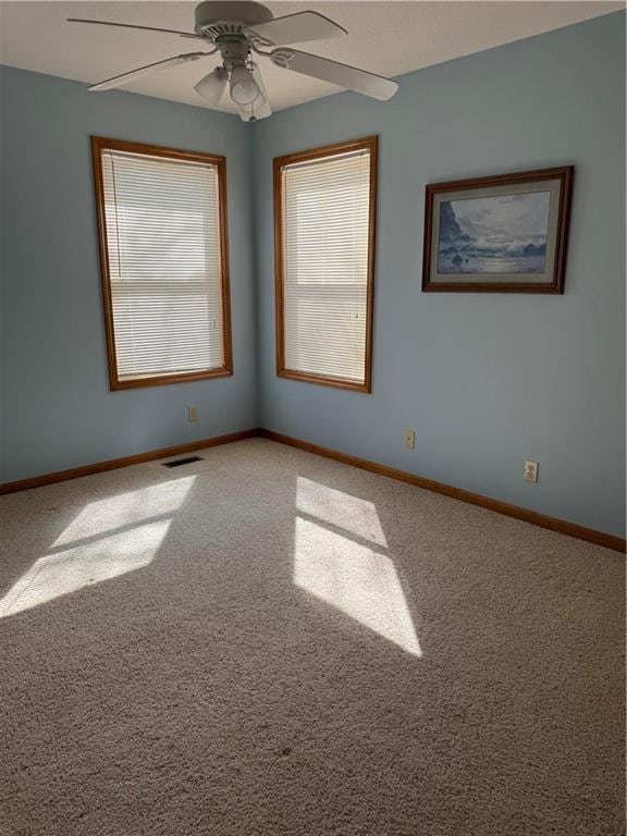 carpeted empty room with visible vents, a ceiling fan, and baseboards