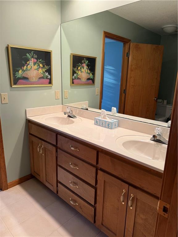 bathroom featuring tile patterned flooring, a sink, baseboards, and double vanity