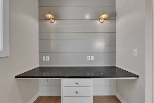 kitchen with dark stone counters, white cabinets, built in desk, and wood finished floors