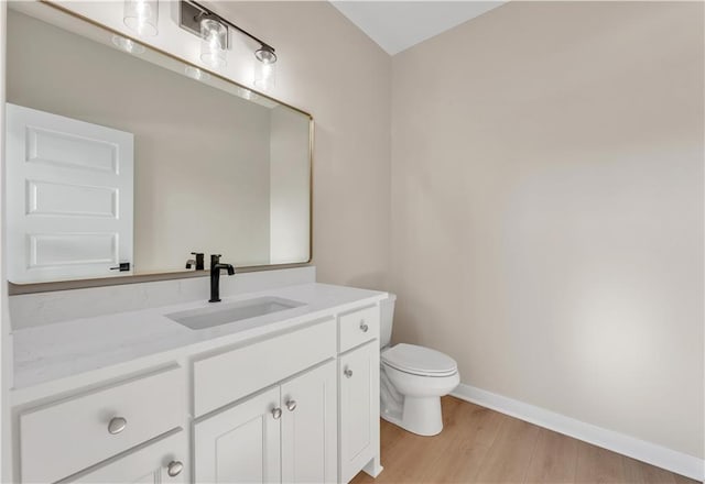 half bathroom with baseboards, vanity, toilet, and wood finished floors