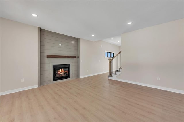 unfurnished living room with light wood-style flooring, a fireplace, stairway, and baseboards