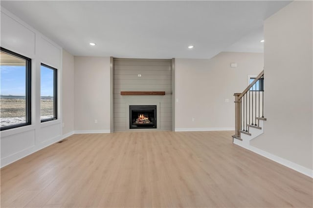 unfurnished living room with visible vents, light wood-style floors, a large fireplace, baseboards, and stairs