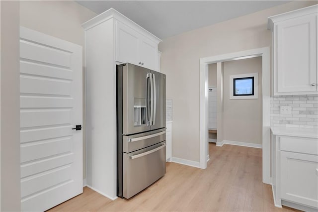 kitchen featuring stainless steel refrigerator with ice dispenser, tasteful backsplash, light countertops, light wood-style flooring, and white cabinetry