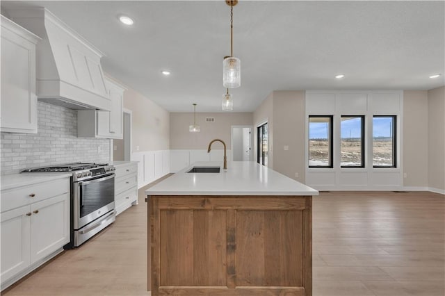 kitchen with tasteful backsplash, stainless steel gas range, a sink, and light wood-style flooring