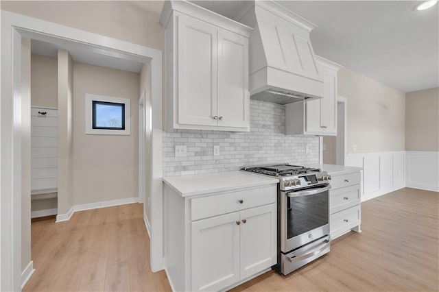 kitchen featuring white cabinets, light wood-style flooring, stainless steel gas range, custom exhaust hood, and light countertops