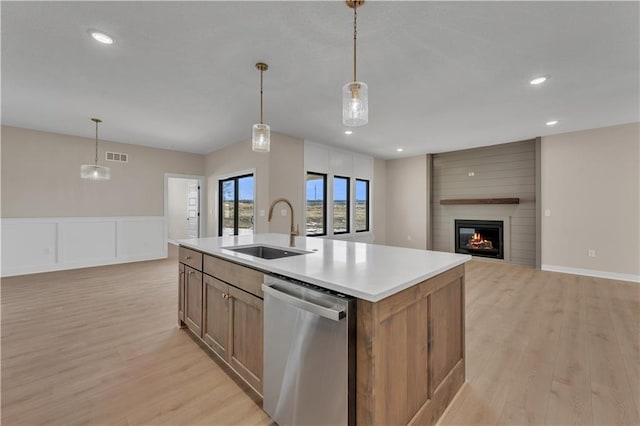 kitchen with a large fireplace, a sink, light wood-type flooring, dishwasher, and an island with sink