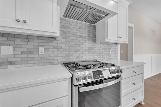 kitchen with decorative backsplash, stainless steel gas stove, white cabinets, light wood-type flooring, and premium range hood