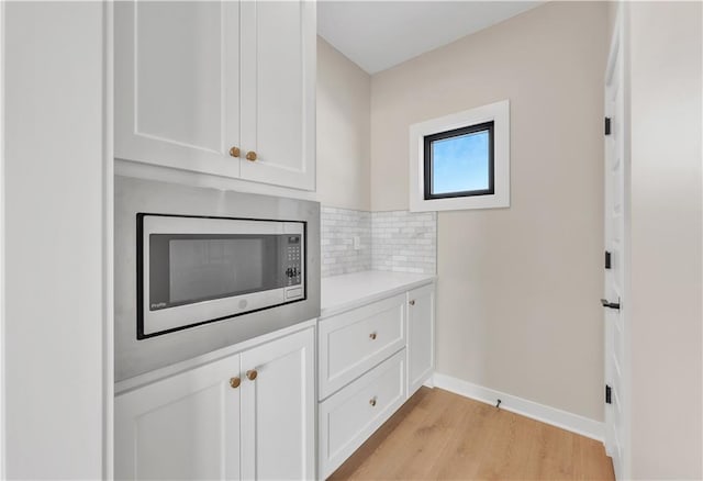 interior space with light wood finished floors, white cabinets, decorative backsplash, stainless steel microwave, and light countertops