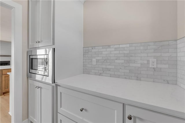 kitchen featuring light stone counters, tasteful backsplash, stainless steel microwave, light wood-style floors, and white cabinets