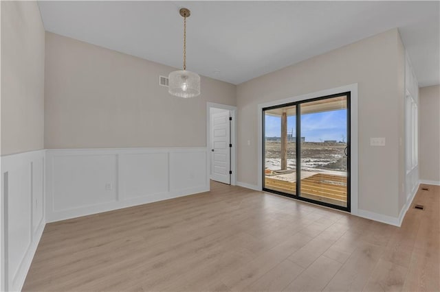 empty room with light wood finished floors, visible vents, a decorative wall, and a wainscoted wall